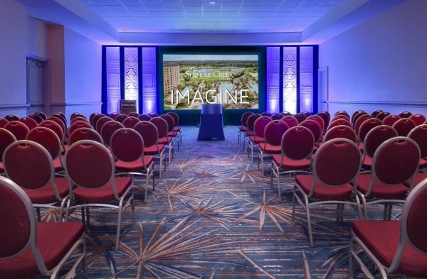 A smaller meeting space with rows of red cushioned chairs facing a large screen at the head of the room surrounded by blue LED uplighting. 