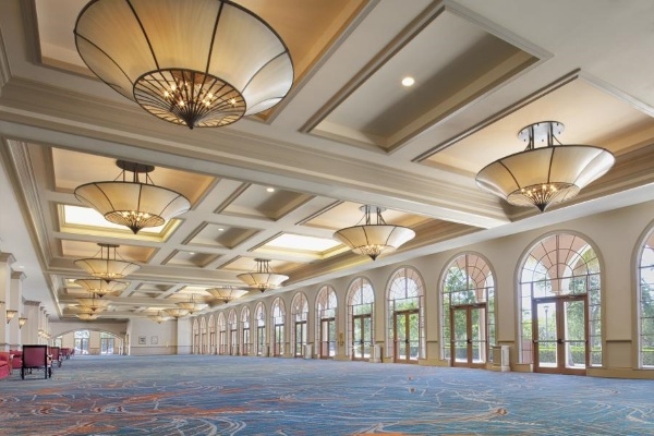 A grand lobby with a long wall of arched glass doorways, an ornate tray ceiling, and large dramatic light fixtures. 