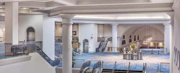 A view of the rotunda reception space with blue carpet, escalators, grand white pillars, and beautiful chandeliers. 