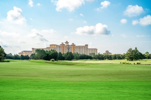 A wide shot with a large hotel in the distance surrounded by blue sky and rolling green fields.