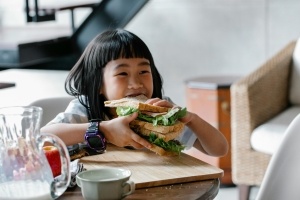 A little girl stuffing her face with a big sandwich at a food hall.
