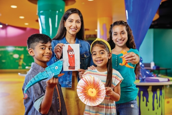 A woman and three children hold handmade art projects while smiling at the camera. 