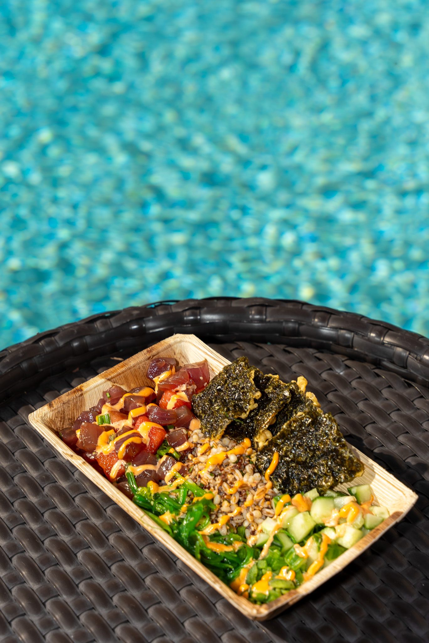 A rectangular dish of food on a table overlooking a glimmering pool. The Tuna Poke at Cat-Tails is a great dish for your healthy New Year's resolutions.