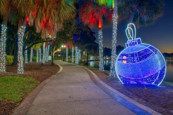 A pathway through palm trees lit with Christmas lights and a giant blue lit ornament