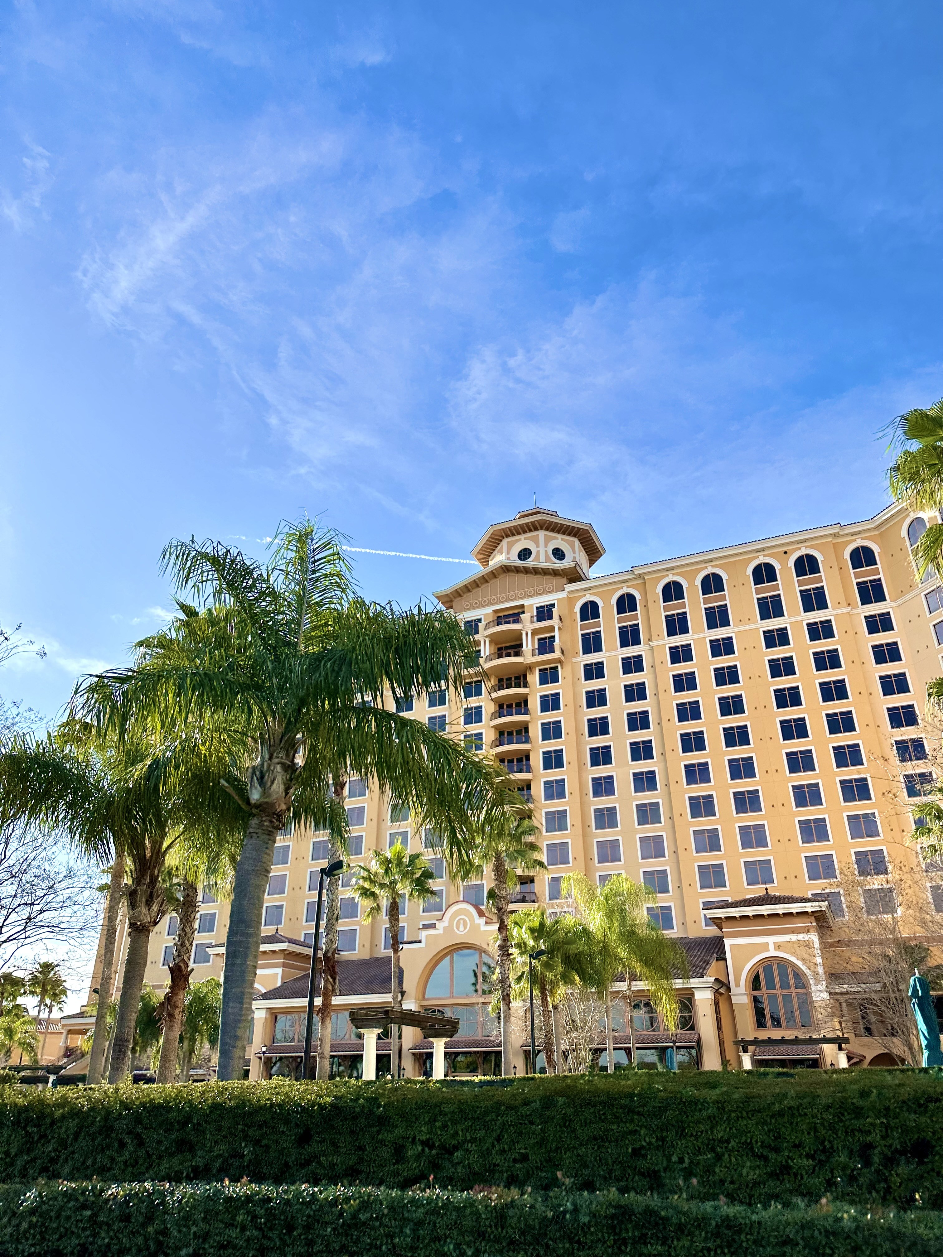 An image of the facade of Rosen Shingle Creek hotel showing hundreds of hotel windows, palm trees and green bushes lining the front of the building. 