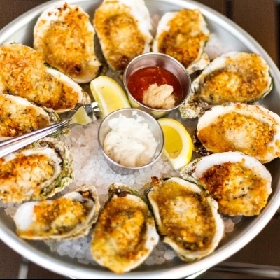 A circle of breaded oysters on a plate of rushed ice with mayo, lemon wedges, and cocktail sauce. 