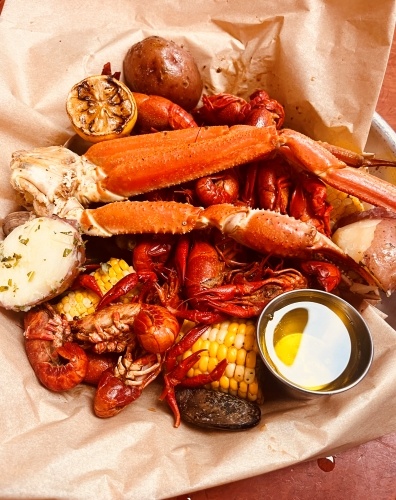 Crawfish, crab legs, corn on the cob, and a side of butter on brown parchment paper. Visit Reel Fish for fresh seafood in Orlando.