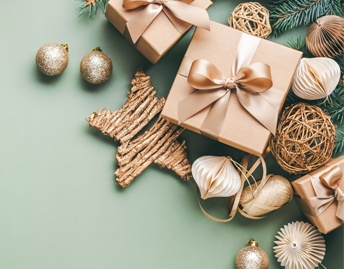 A green background with wicker and gold Christmas ornaments, brown and gold wrapped presents, and pine boughs