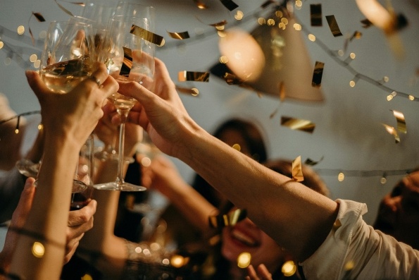 Hands hold glasses of Champagne together in a toast surrounded by falling gold confetti. 