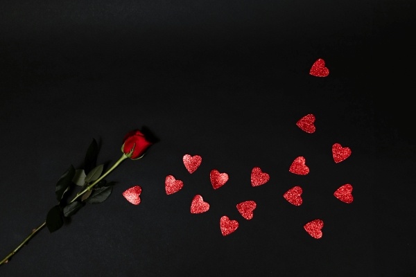 A single red rose and small shiny red hearts against a black backdrop. Celebrate Valentine's Day at Rosen Shingle Creek.