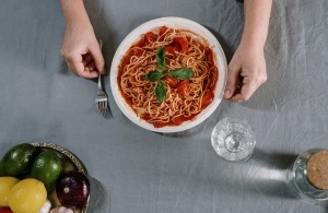 A bowl of spaghetti and meatballs on a table with hands and a fork preparing to eat. Find dishes like this among the best Italian restaurants in Orlando.